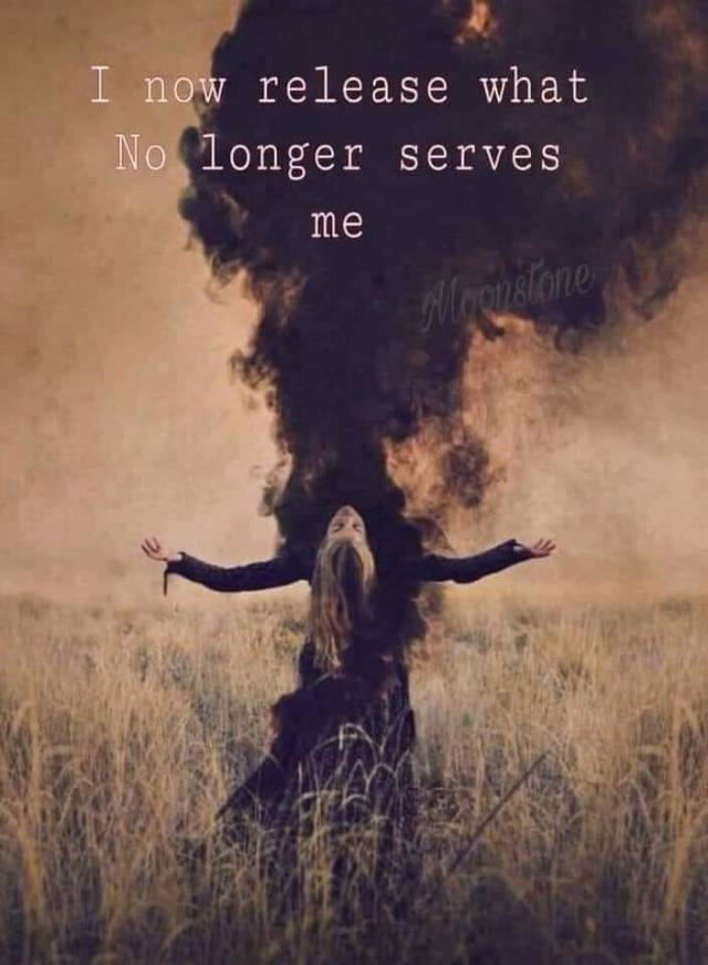 A woman in a flowing black dress stands in a field, arms outstretched towards a dark cloud of smoke above her. The background features tall grass and a muted sky, with the words 'I now release what no longer serves me' overlaying the image.
