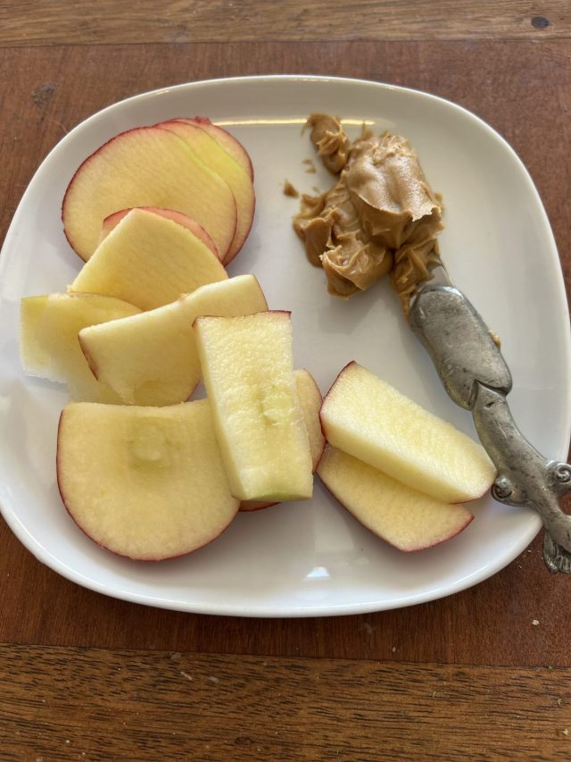 A plate featuring sliced apples in various shapes and sizes alongside a scoop of peanut butter and a small silver spoon.